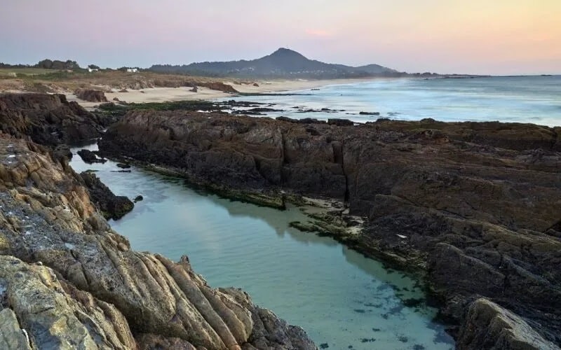 A blue pond between rocks and the beach in the background