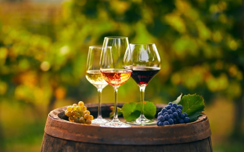 Three glasses of wine and grapes on a barrel