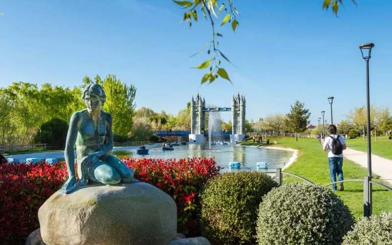 A park with a river, a sculpture and a bridge crossing a river