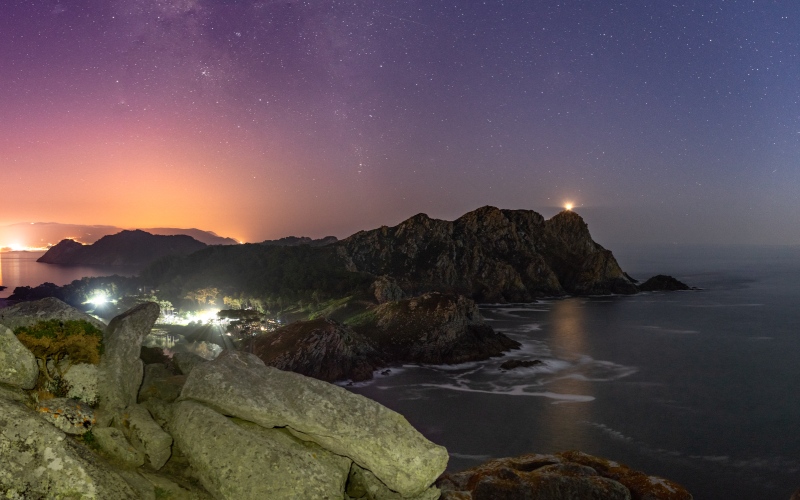 A panoramic view of the islands and a lit lighthouse under the stars