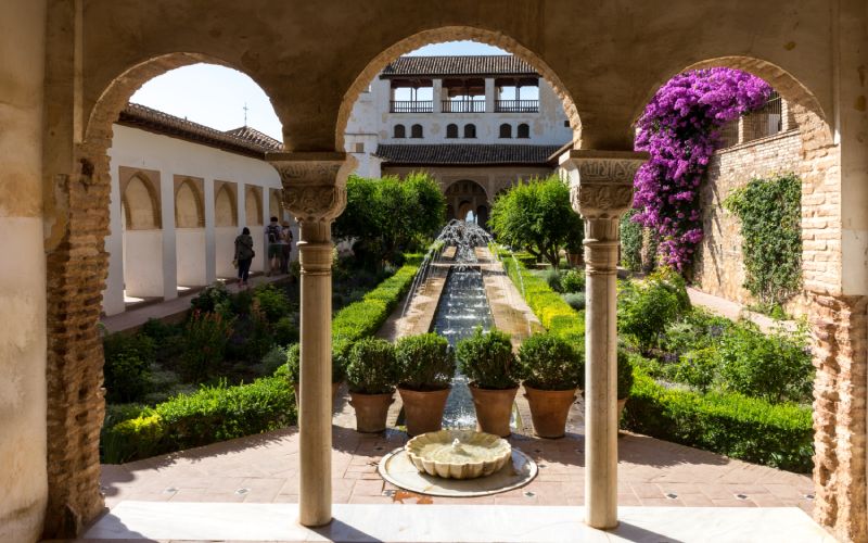 A courtyard with a pond, a fountain and beautiful plants surrounded by columns and arcades
