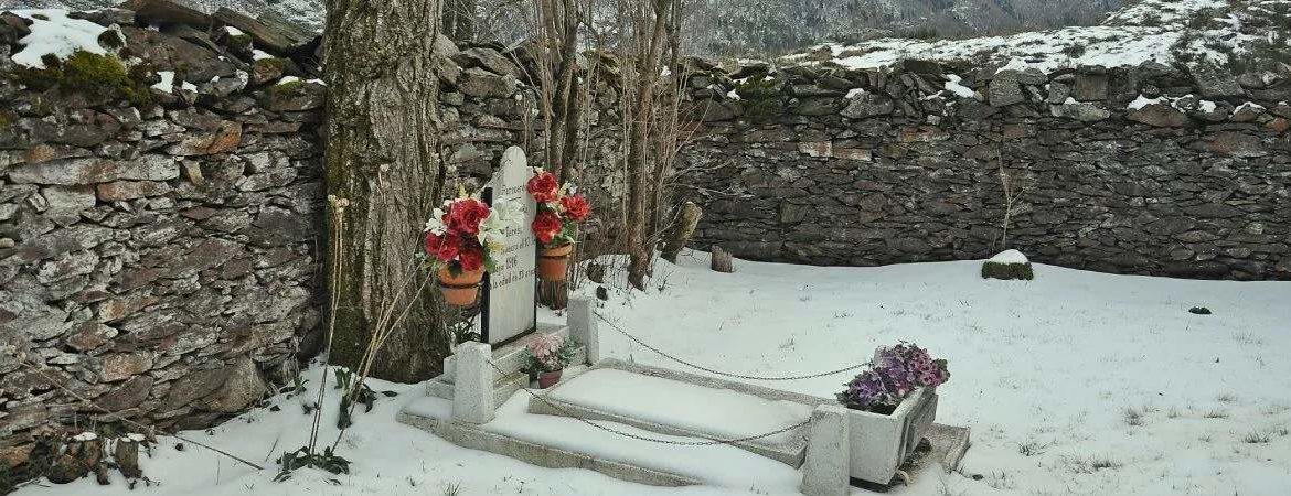 A solitary tombstone, with flowers, and snow around it