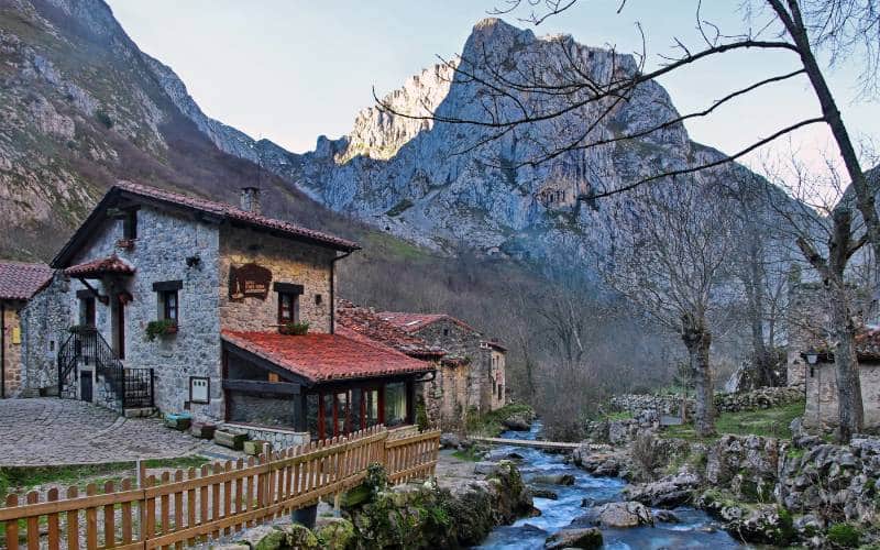 Stone houses in Bulnes next to a creek and a mountain in the background