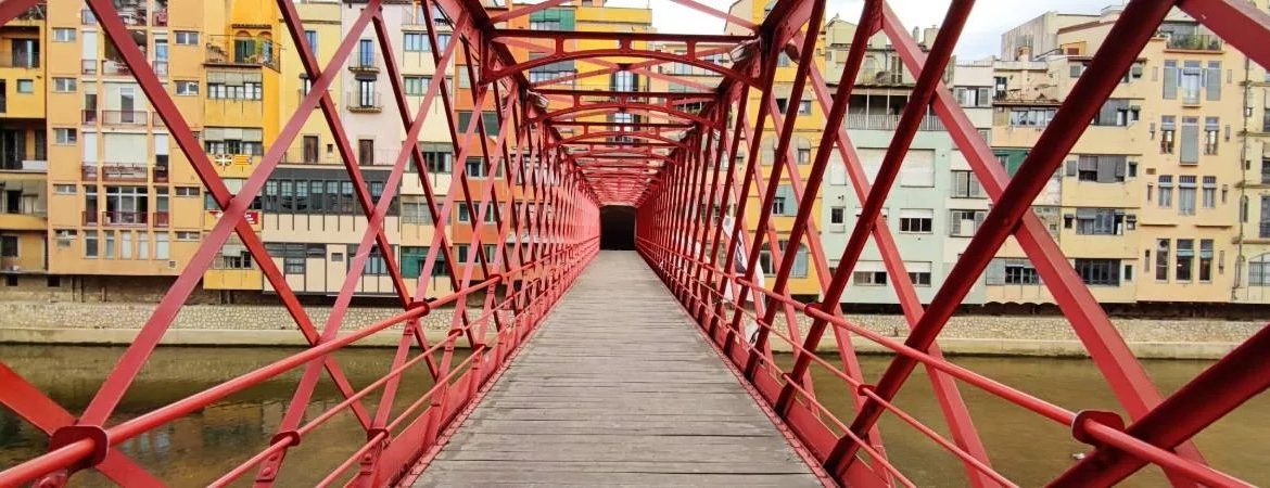 A red bridge over a river, with colourful buildings in the background