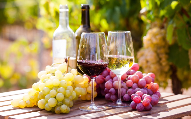 Two glasses of wine and white and red grapes on a wooden table