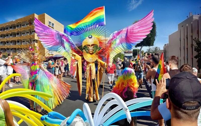 A colourful parade, and someone with wings and the rainbow flag in the middle