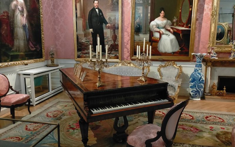 A museum room with paintings and a piano