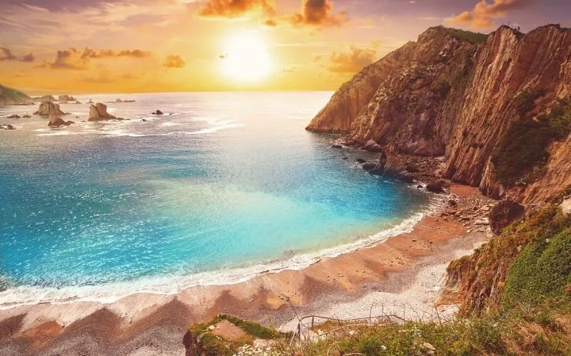 The sun setting on a beautiful beach with a cliff on the right