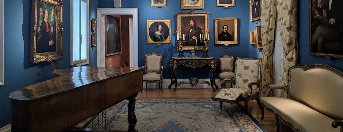 A room with paintings on the walls, a piano and old furniture
