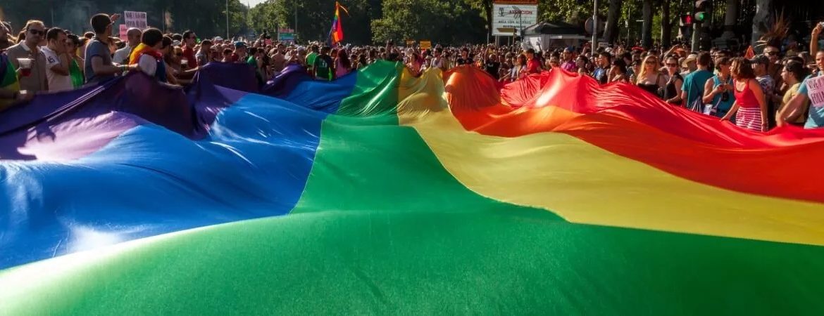 A large rainbow flag carried by a crowd of people