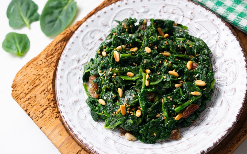 A dish with spinach, pine nuts and raisins on a white plate