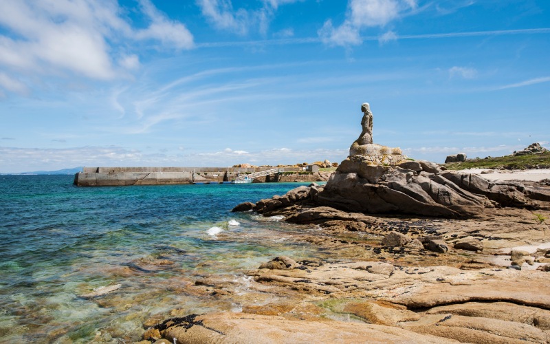 A sculpture of a mermaid on a rock facing the sea